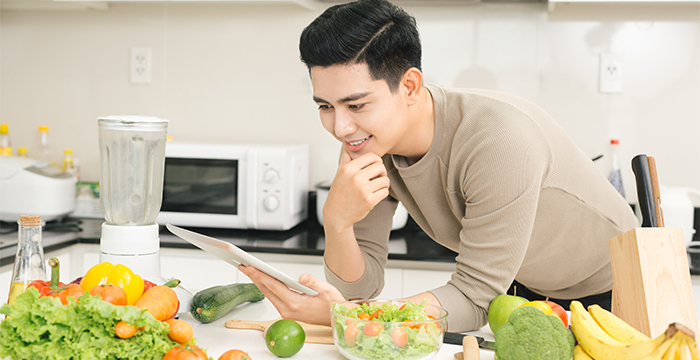 Asian man holding tablet while cooking in kitchen